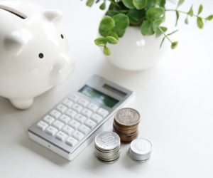 a white piggy bank, white calculator, and coins on top of a white table