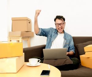 man sitting on the couch happily raising his hand while looking at his laptop