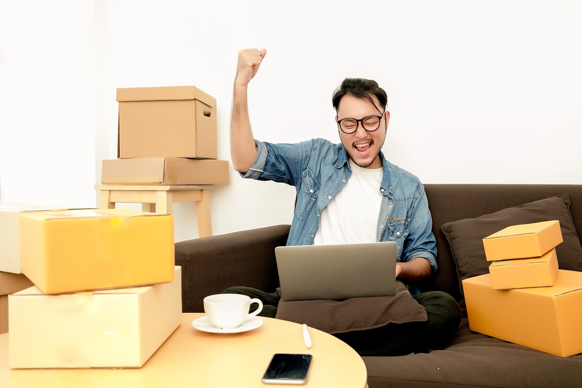 man sitting on the couch happily raising his hand while looking at his laptop
