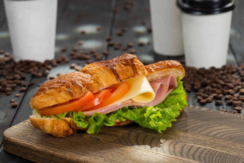 sandwich with ham, cheese, tomatoes and lettuce on a cutting board
