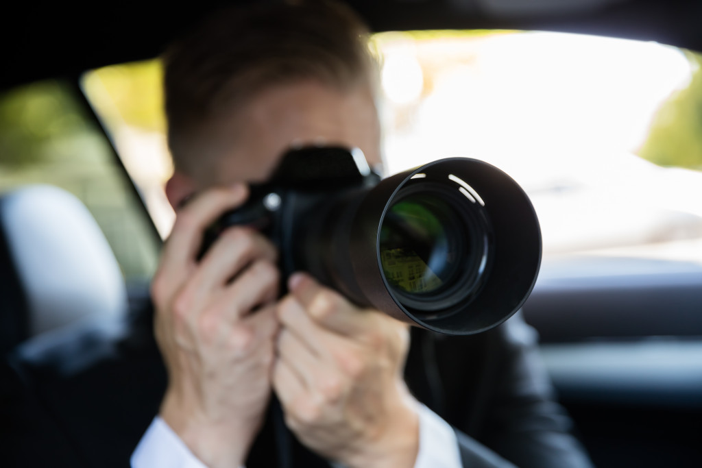 A man in a car using a camera with high-definition lens to photograph something or someone