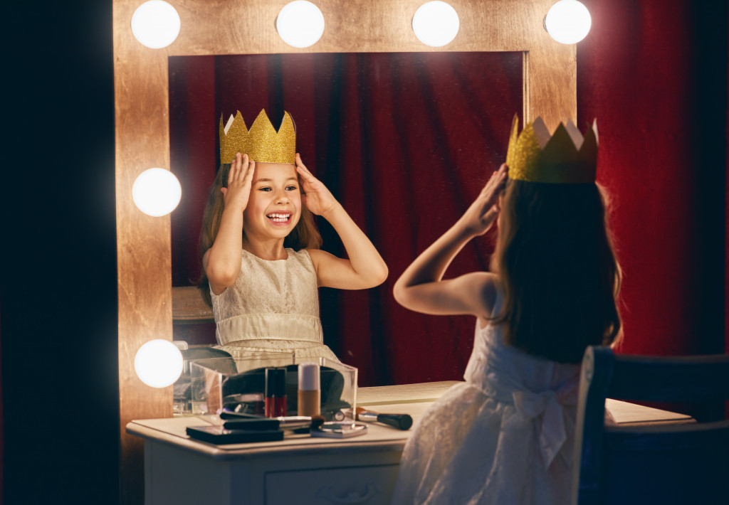 A child looking at a theater makeup mirror while wearing a fake crown